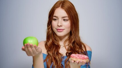Doubt female person making a decision in studio. Girl choosing doughnut indoors