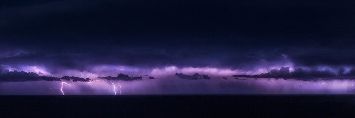 A panorama of a lighting storm out to sea lighting up the clouds and with fork lightning