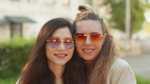 Best friends girls hug, smile and show positive face emotions. Portrait of two young smiling hipster women wearing sunglasses of heart shape.