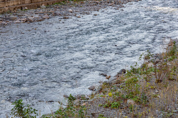 Strong water flow of a mountain river near a rocky shore
