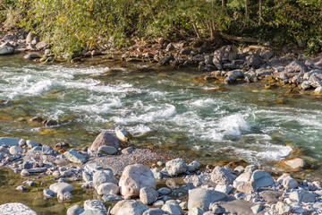 Strong water flow of a mountain river near a rocky shore