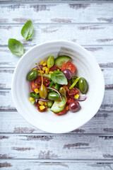 Simple Salad with Green and Kalamata Olives, Cucumber, Cherry and marinated Tomatoes, Capers and Jalapeno Pepper. Bright wooden background. Top view.	
