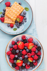 Fresh berry salad on blue dishes. Vintage wooden background.