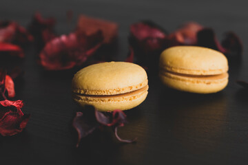 Close-up of breakfast morning with yellow macaroons lemon taste. close-up of french dessert on the black background and flowers around in a simple vintage composition. Food photography
