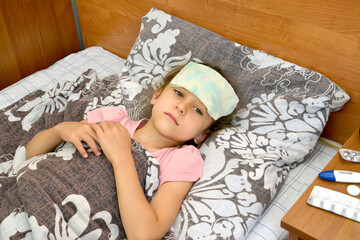 The sick girl lies in bed with a compressor on her head. Treatment