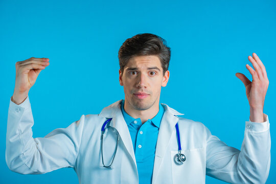 Handsome Bored Doctor Man In Medical Coat Showing Bla-bla-bla Gesture With Hands And Rolling Eyes Isolated On Blue Background. Empty Promises, Blah Concept. Lier.