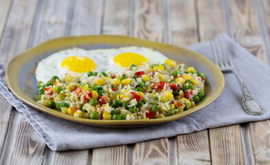 Rice with vegetables pepper, peas, corn and fried eggs on a plate. Place for text.
