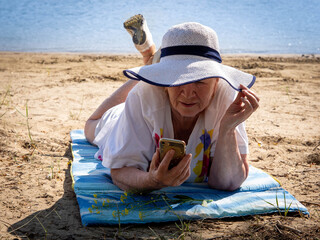 Pensive elderly woman, elderly pensioner, rest on the sand by the river, the concept of time and age, summer vacation in the fresh air, healthy lifestyle