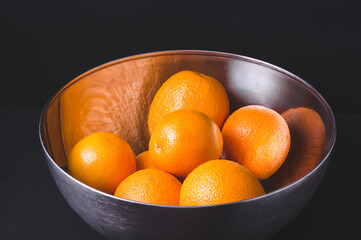 Fresh juicy oranges in a steel bowl in black background.Citrus fruits.Vitamin C fruits