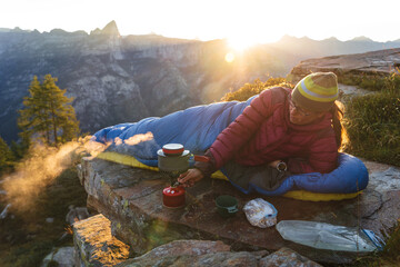 A woman cooking breakfast from her bivouac on a beautiful morning in the mountains.