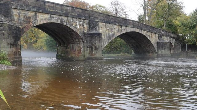 Large stone bridge crossing the river ribble near Clitheroe. Edisford bridge with slow flowing water in Autumn