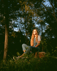 Girl in the woods wearing denim overalls and a cowboy fedora hat. Autumn vives.