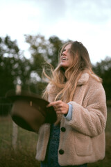 Girl in the woods wearing denim overalls and a cowboy fedora hat. Autumn vives.