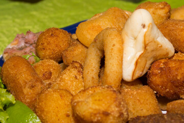 CLose-up photograph of tasty party snacks. Fried Onion, Mini Pizza, Chicken drumstick, meat drumstick, sfiha, lettuce and lemon to accompany.