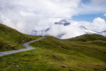 Walking path in the Valais Alps near First, Switzerland with Jungfrau mountain covered by clouds in the distance. 