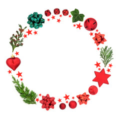 Abstract Christmas wreath decoration with cedar, fir & ivy leaves with baubles, bows & red stars on white background. Festive composition for the holiday season. Flat lay, top view, copy space.