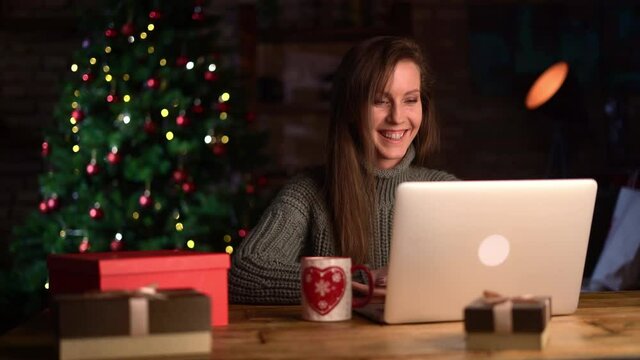 Young woman at home in Christmas time talking on video chat online on laptop computer. Happy and smiling, christmas tree in background.