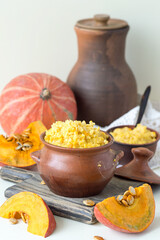 Millet porridge with pumpkin in a small clay pot on an old table. Selective focus.