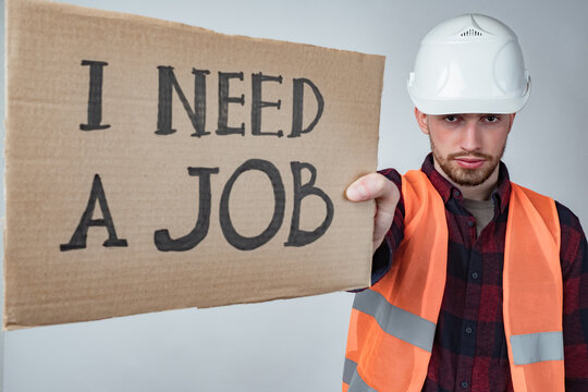 I need a job. A man shows a sign that says i need a job. Concept - builder was left without work. Unemployed builder on a gray background. Man in the orange vest symbolizes the blue-collar worker.