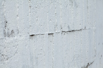 Part of a close-up concrete wall with cracks, covered with white paint. Urban texture.