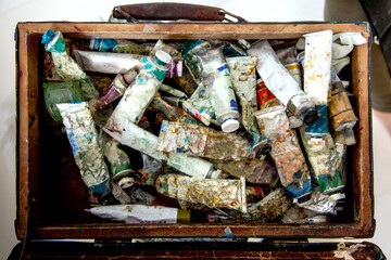 Painter hands picking oil paint tube from collection of neglected and messy artist oil paint tubes