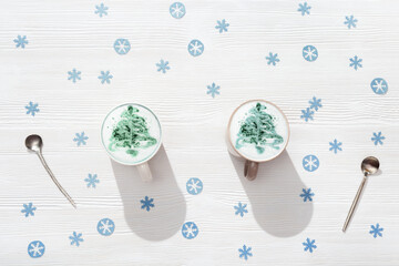 Naklejka premium Top view of cup of coffee cappuccino with pattern New Year tree on white wooden table decorated blue snowflakes.