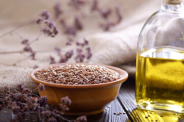 Flax oil and raw seeds in wooden bowl on kitchen table closeup