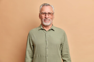 Portait of handsome European elderly man smiles positively enjoys retirement wears shirt and...