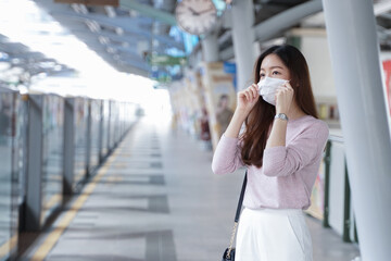 Asian business woman in casual clothes wearing face mask. She is waiting for the train to go to work on the platform station. New normal lifestyle in city concept.