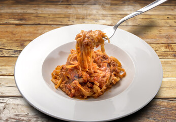 spaghetti egg based (Italian tagliatelle) topped with meat and tomato sauce, steamed in a plate on rustic wooden background