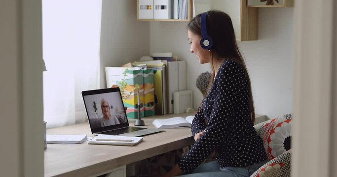Smiling young woman wearing wireless headphones, holding video call with elderly mother, enjoying pleasant conversation. Happy grown up daughter making bye-bye gesture, finishing distant talk with mum