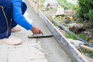 Worker, labor or mason is sitting and repairing or constructing walkway or pathway by using trowel plastering cement concrete. Concept of construction site.