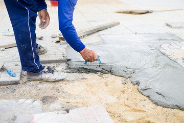 Worker, labor or mason is repairing or constructing walkway or pathway by using trowel plastering mixed cement concrete. Concept of construction site and repairing renovating work.