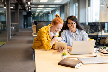 Two young laughing intercultural businesswomen looking at tablet screen