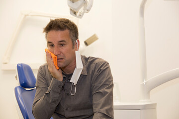 Hombre en la consulta del dentista con dolor de muelas y mascarilla higiénica por la pandemia ...