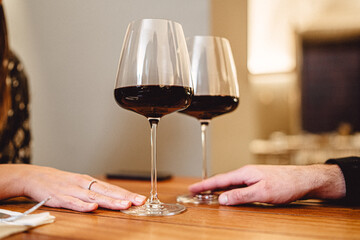 Two wineglasses touching at table. Love and romance concept of a loving couple celebrating their meeting in a restaurant toasting with red wine. Closeup of the glasses