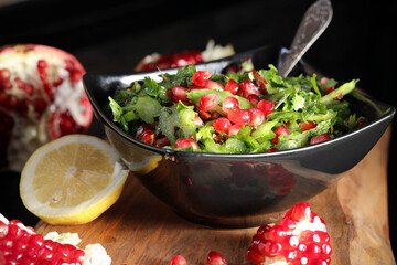 Tabbouleh with pomegranate. Green salad of parsley and herring with large pomegranate grains, in a black plate on a dark background and a wooden board.