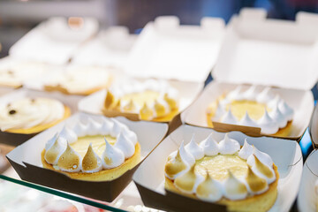Showcase with cakes decorated with fried meringues. White mousse cake.