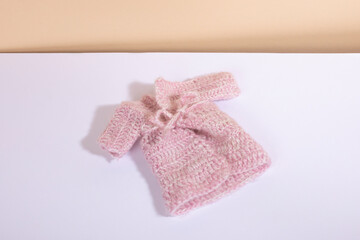 A small cosy warm hand knit pink sweater for newborn babies laying on a white background and a beige bakground. Handmade clothes for children