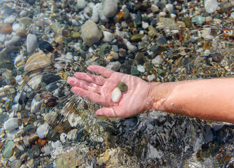 Women's hand holds sea stones in the clear sea water.  Crystal clear sea water through which you can see the stones lying on the bottom.  Top view. Shot in the Turkey, Kemer, Kirish