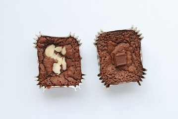 Home made chocolate brownies with sliced macadamia and brown chocolate fragment on top.  Chocolate baked confections in aluminum foil mould for dessert menu image on white background.
