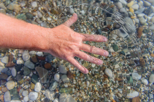 Man's hand feeling the water. 
Crystal clear sea water through which you can see the stones lying on the bottom.  Top view. Shot in the Turkey, Kemer, Kirish