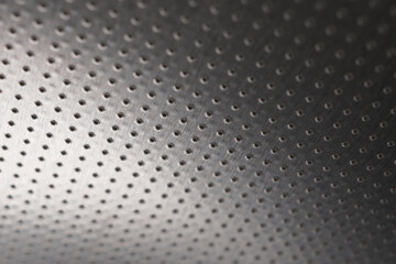 Dark metal wallpaper or background. Perforated aluminum surface with many holes, hanging from above like a ceiling. Perforation rows go into the distance and form perspective