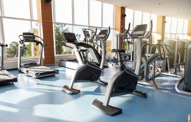Fototapeta na wymiar Interior of a modern gym fitness room with large windows. Treadmills and exercise bikes