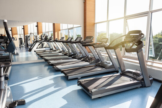 Interior of modern gym fitness room with large windows and treadmills
