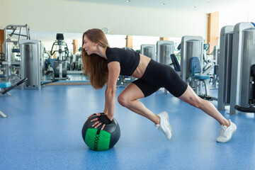 Young sportive fit woman trains with medicine ball in a modern light gym. Cross training