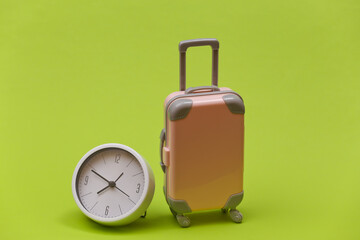 Time to travel. Mini plastic travel suitcase and clock on green background. Minimal style
