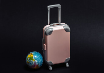 Travel or trip concept. Mini plastic travel suitcase with globe on black background.