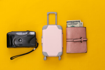 Travel flat lay. Mini plastic travel suitcase, purse and camera on yellow background. Minimal style. Top view