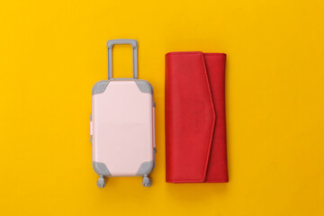 Travel flat lay. Mini plastic travel suitcase, red wallet on yellow background. Minimal style. Top view